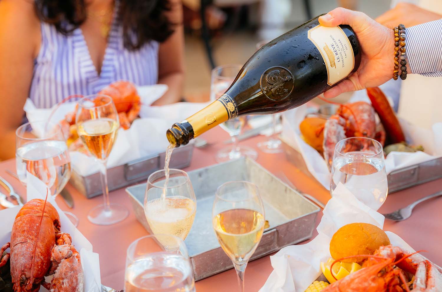 Bottle of Le Reve being poured into sparkling wine flutes with lobster on table