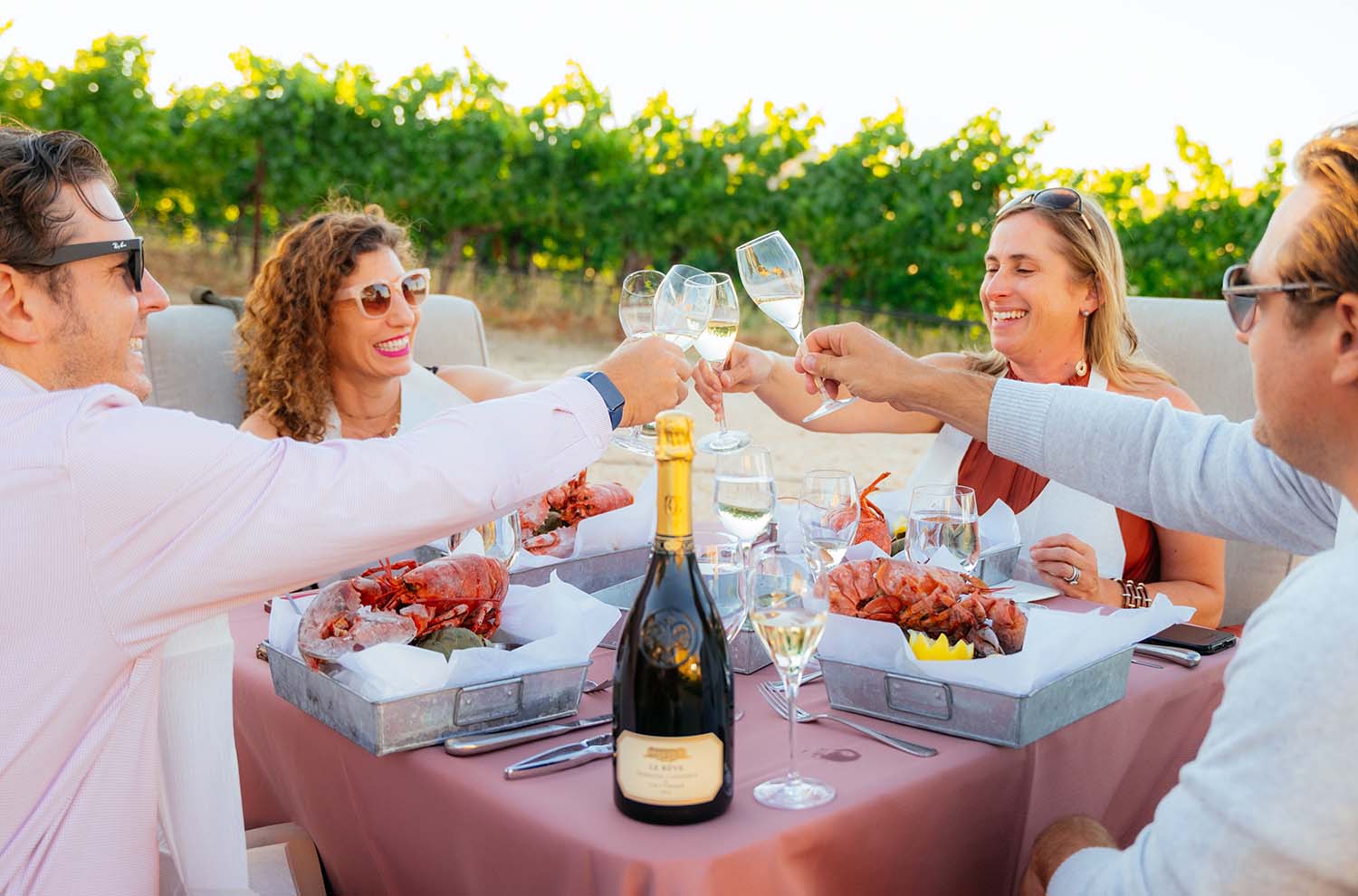 a bottle of Le Reve on table outdoors with four people toasting