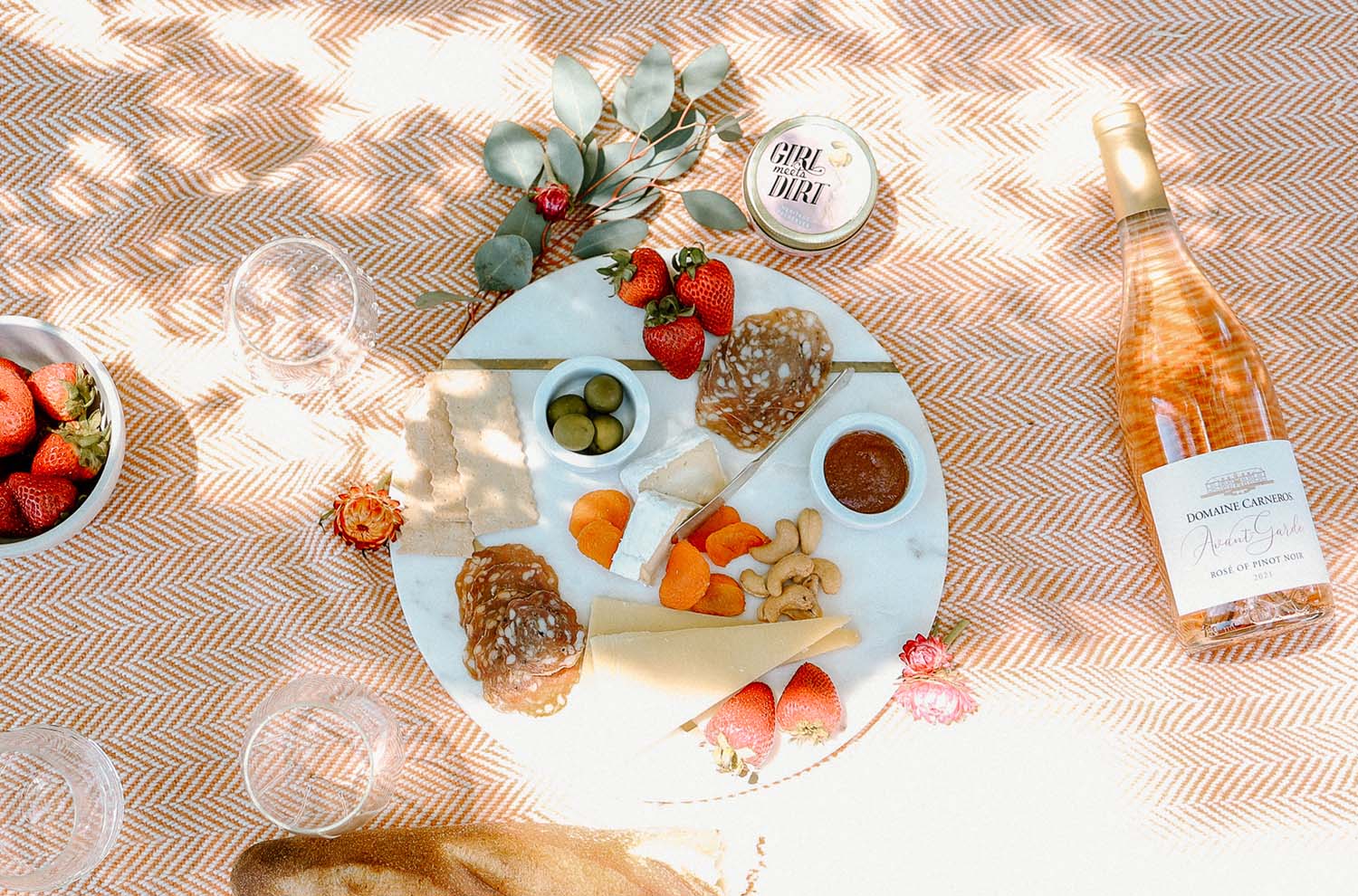 picnic blanket with bottle of rose, cheese board, bowl of strawberries
