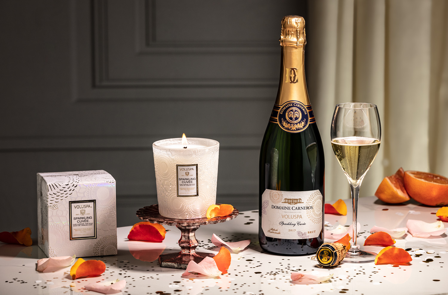 Volsupa candle and sparkling wine on a marble countertop with floral petals and glitter.