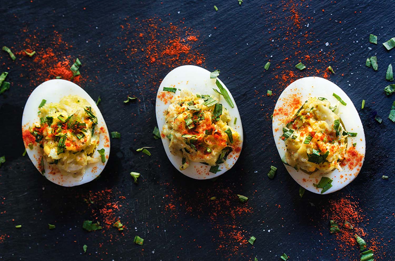 three deviled eggs on black plate seasoned with cayenne pepper