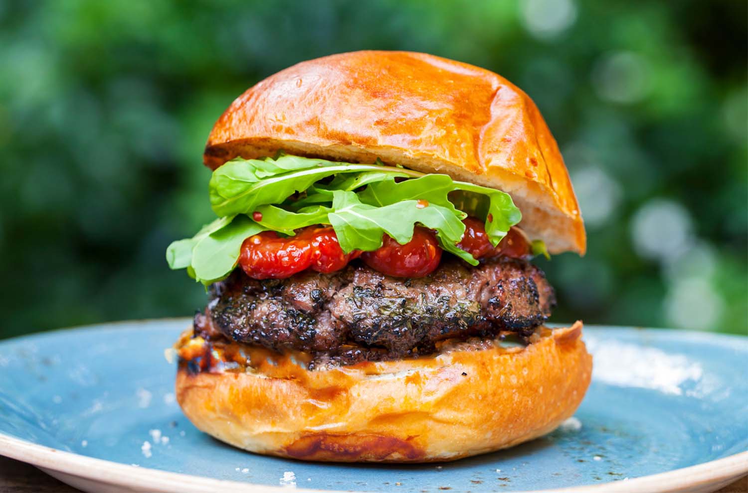 Burger with brioche bun, red sauce, arugula on blue plate