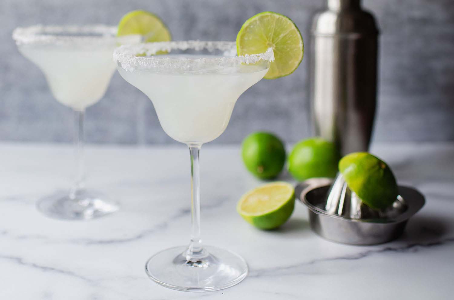 Two margarita glasses with shaker and lime in background