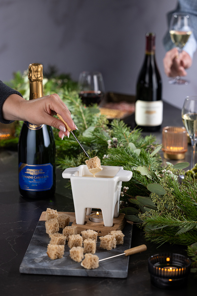 Hand dipping into Fondue pot with sparkling wine on table