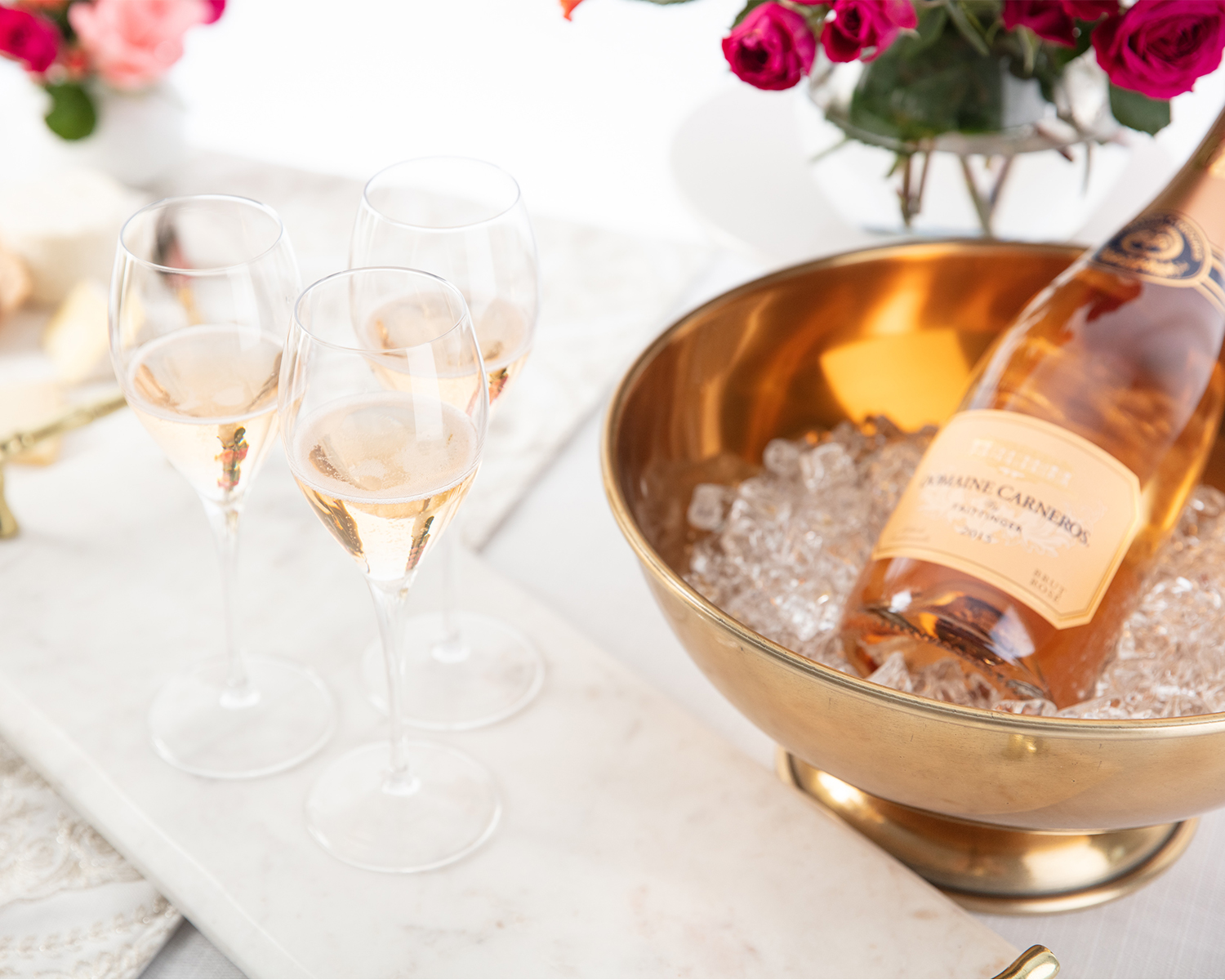 Rosé sparkling wine in a gold ice bucket with three flutes of wine next to it